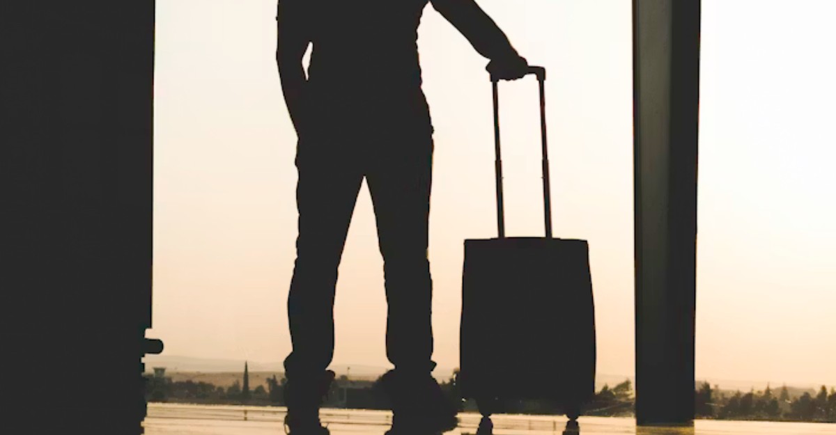 A man standing with his luggage at an airport. (Photo: Yousef Alfuhigi / Unsplash)