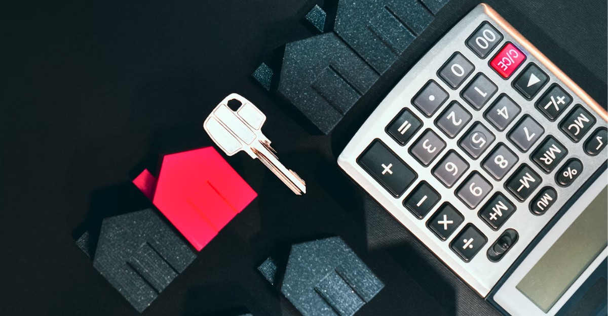 A photo of small houses, a key, and a calculator on a table. (Photo: Jakub Żerdzicki / Unsplash)