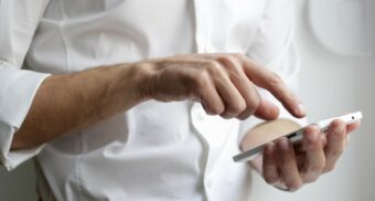 A person in a white dress shirt interacting with a phone. (Photo: NordWood Themes / Unsplash)