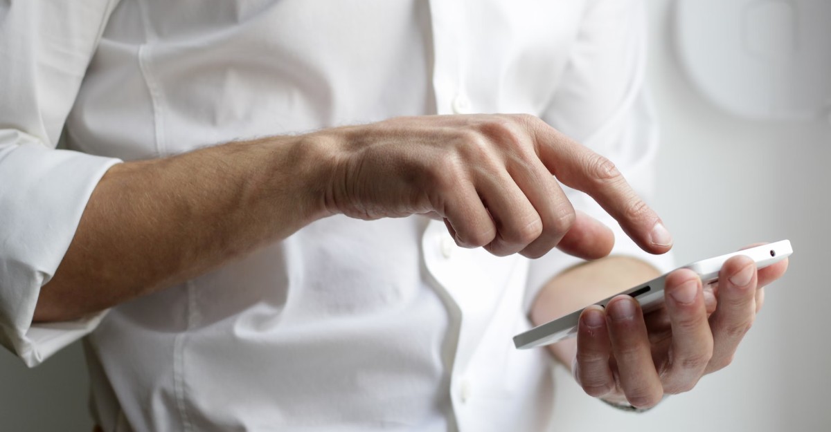 A person in a white dress shirt interacting with a phone. (Photo: NordWood Themes / Unsplash)