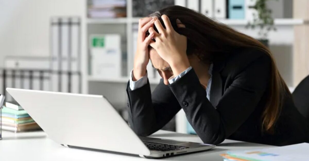 A worker runs her hands through her hair while sitting in front of a laptop. (Photo: Depositphotos)