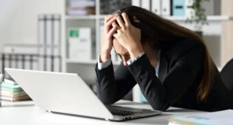 A worker runs her hands through her hair while sitting in front of a laptop. (Photo: Depositphotos)