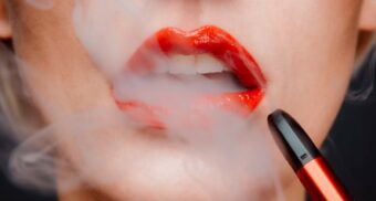 A woman with red lipstick using a vape. (Photo: Chiara Summer / Unsplash)