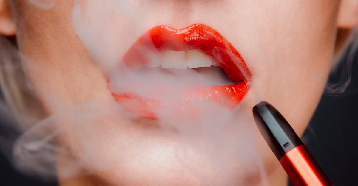 A woman with red lipstick using a vape. (Photo: Chiara Summer / Unsplash)