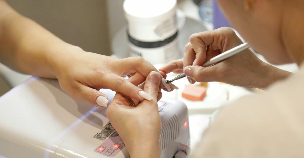 A nail salon employee applies nail polish to a customer's fingernails.