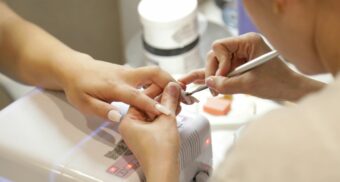 A nail salon employee applies nail polish to a customer's fingernails.
